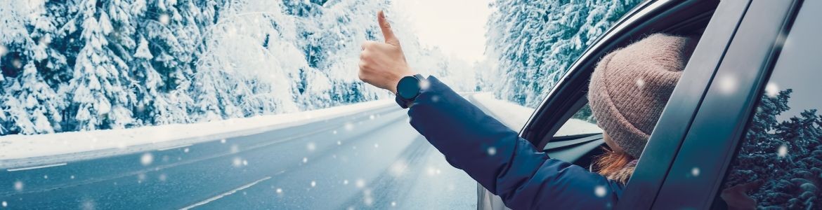 mulher feliz a gesticular no carro numa estrada com neve